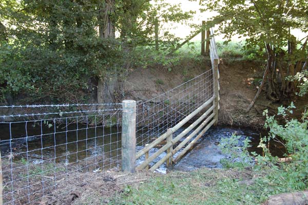 Stream crossing with swinging rails for flood water to pass through.